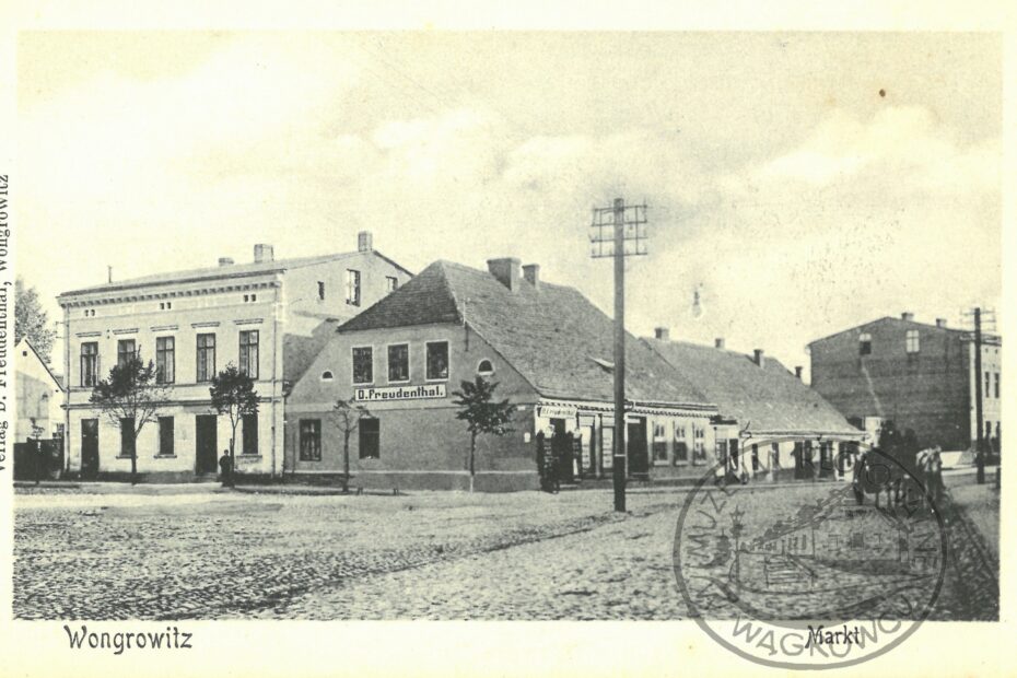 Widokówka przedstawiająca fragment wągrowieckiego rynku z pocz. XX w. W centralnej części przysadzisty budynek z dachem naczółkowym. Na nim napis D. Freudenthal.